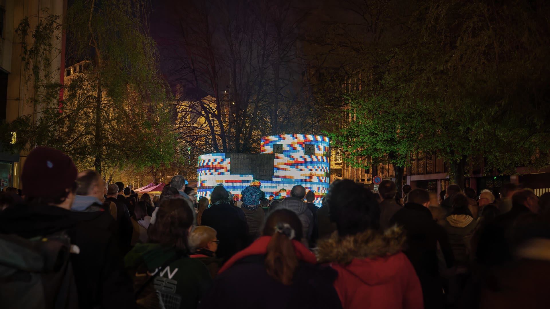 874 seen down the street with a dense crowd watching from behind, the shaft carrying a red, white and blue chevron pattern, bare and leafed trees framing it on both sides